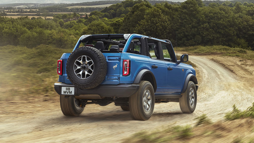 „Ford Ford Bronco von hinten in der Natur, unterwegs auf einer sandigen Straße zwischen grüner Vegetation“